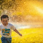 Kid-friendly Backyard - a young boy running through a sprinkle of water