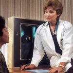 Health Monitoring - doctor sitting on desk talking to sitting woman