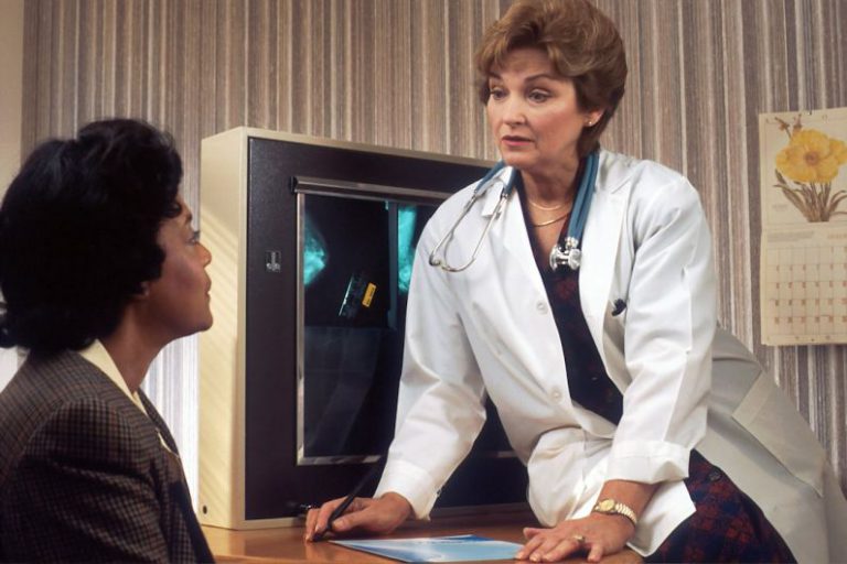 Health Monitoring - doctor sitting on desk talking to sitting woman